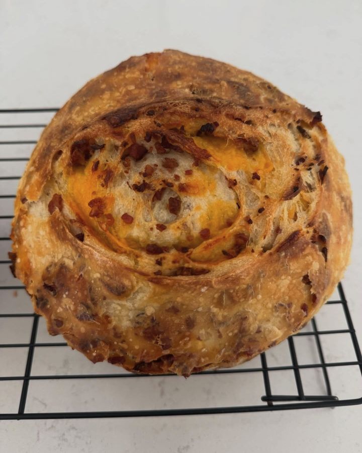 A bacon cheddar swirl sourdough loaf cooling on a black wire rack